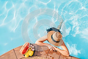 Woman in straw hat and bikini in sunglasses at swimming pool enjoying fresh tropical fruits