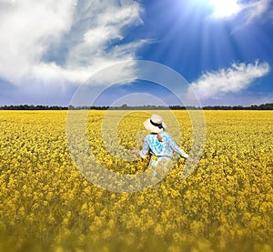 Woman in a straw hat and a blue dress on a wild field blossom yellow flowers and a bright sky with white clouds summer nature land