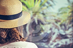 Woman in a straw hat holding in a hand royal dates fruit in a bowl of coconut in a palm tree grove.