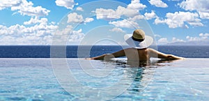 woman with straw hat in infinity swimming pool with sea view at luxury resort. summer vacation background