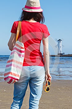 Woman in straw hat with material bag and sunglasses on west breakwater in Swinoujscie. Characteristic navigational mark Windmill