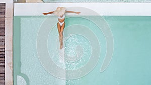 Woman in straw hat relaxing in clear pool water in hot sunny day on Bali villa