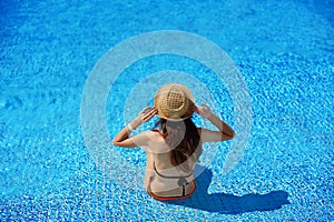 Woman in a straw hat relaxing on a deck-chair near a luxurious summer pool in hotel, concept time to travel with space