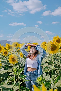 A woman in a straw hat is standing in a large field of sunflowers. stands in flowering field. Summer time, lifestyle, travel and