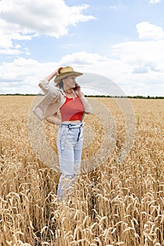 woman in straw hat talking on cellphone while walking on wheat field at summer day