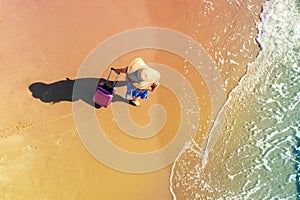 Woman in a straw hat with a travel suitcase walks on the. Top view