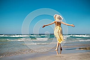 Woman with straw hat and yellow dress on the beach and arms streched