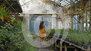 Woman in straw hat and yellow dress running in big industrial hothouse.