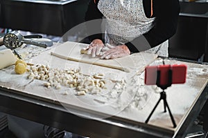 Woman streaming online italian cooking lesson of gnocchis with mobile phone inside pasta factory - Focus on hands