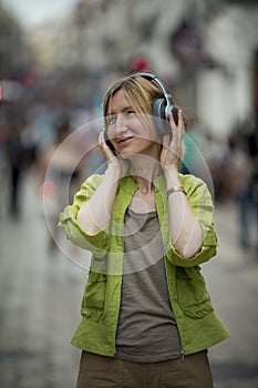 A woman on the street enjoying music with headphones.