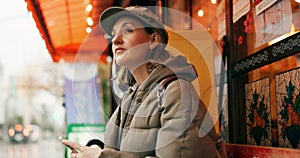 Woman, street and waiting for taxi with phone in rain, thinking or winter for travel, transport and cab in city. Girl