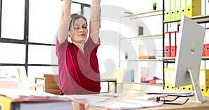 Woman stretches stretches her arms up at workplace in office