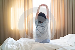 Woman stretching in bed in front of window with curtains