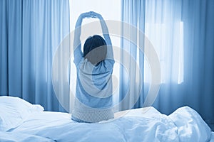 Woman stretching in bed in front of window with curtains