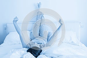 Woman stretching in bed with legs raised up high in bedroom