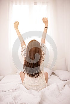 Woman stretching in bed after wake up, back view