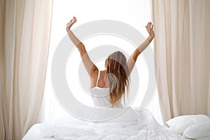 Woman stretching in bed after wake up, back view, entering a day happy and relaxed after good night sleep. Sweet dreams