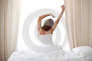 Woman stretching in bed after wake up, back view, entering a day happy and relaxed after good night sleep. Sweet dreams