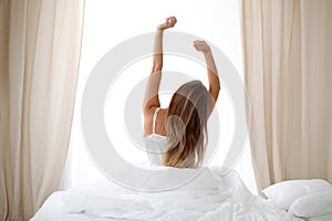 Woman stretching in bed after wake up, back view, entering a day happy and relaxed after good night sleep. Sweet dreams