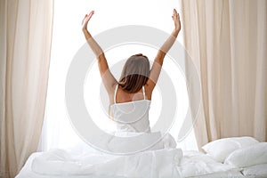 Woman stretching in bed after wake up, back view, entering a day happy and relaxed after good night sleep. Sweet dreams