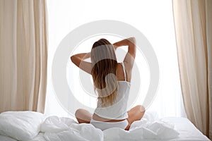 Woman stretching in bed after wake up, back view, entering a day happy and relaxed after good night sleep. Sweet dreams