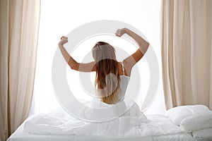 Woman stretching in bed after wake up, back view, entering a day happy and relaxed after good night sleep. Sweet dreams