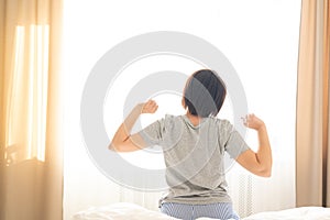 Woman stretching in bed after wake up in front of window, back view