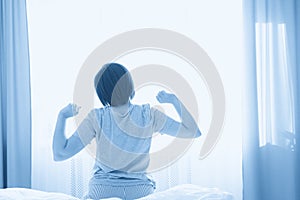 Woman stretching in bed after wake up in front of window, back view