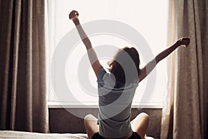 Woman stretching in bed after waking up, back view