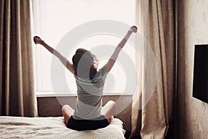 Woman stretching in bed after waking up, back view