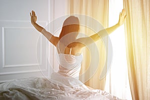 Woman stretching in bed after waking up, back view, entering a day happy and relaxed after good night sleep. Good