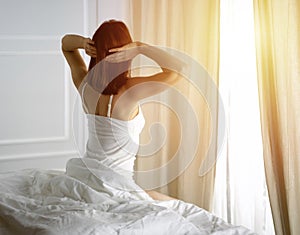 Woman stretching in bed after waking up, back view, entering a day happy and relaxed after good night sleep. Good