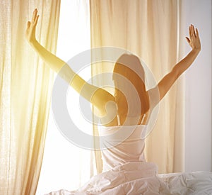 Woman stretching in bed after waking up, back view, entering a day happy and relaxed after good night sleep. Good