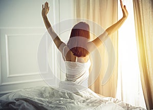 Woman stretching in bed after waking up, back view, entering a day happy and relaxed after good night sleep. Good