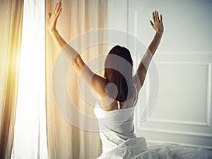 Woman stretching in bed after waking up, back view, entering a day happy and relaxed after good night sleep. Good