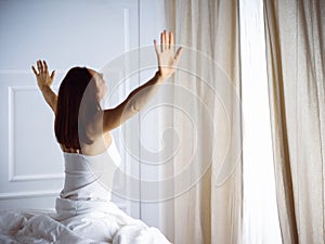 Woman stretching in bed after waking up, back view, entering a day happy and relaxed after good night sleep. Good