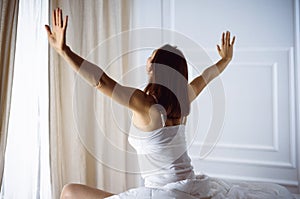 Woman stretching in bed after waking up, back view, entering a day happy and relaxed after good night sleep. Good