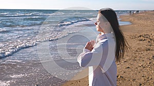 Woman is stretching and doing yoga Namaste Pose on the sand beach with waves, side view.