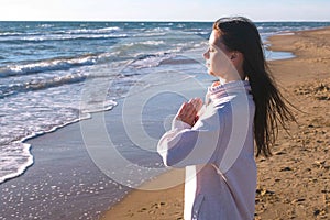 Woman is stretching and doing yoga Namaste Pose on the sand beach with waves, side view.