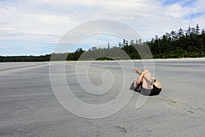 A woman stretching her quads and hips doing yoga on a beautiful sandy beach surrounded by nature