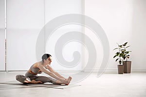 Woman stretching leg in yoga studio. Janu Sirsasana pose variation