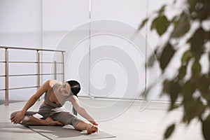 Woman stretching leg in yoga studio. Janu Sirsasana pose variation