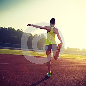woman stretching legs before run during sunny morning on stadium