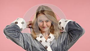 Woman stretching in morning, wearing hood on polka dot robe, relaxed pink background