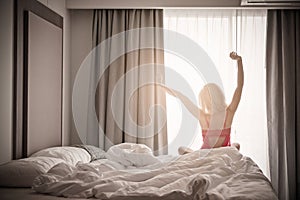 Woman stretching near bed after waking up with sunrise at morning, back view