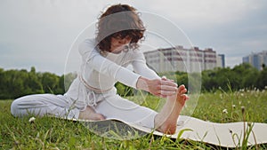 Woman stretching and touch her leg for yoga at the park. Girl in white sportswear lying on caremat develops plasticity