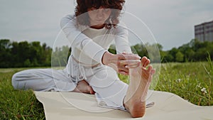 Woman stretching and touch her leg for yoga at the park. Girl in white sportswear lying on caremat develops plasticity