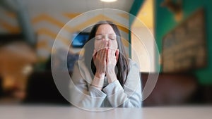 Woman stretching and yawning. Sad woman sitting in a cafe and waiting her order. Closeup.