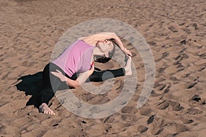 Woman stretching yoga on the beach in the city. Sirsasana, Supta upavistha konasana pose.