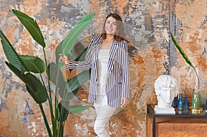 Woman in striped jacked posing in front of big plant. Indoor interior portrait